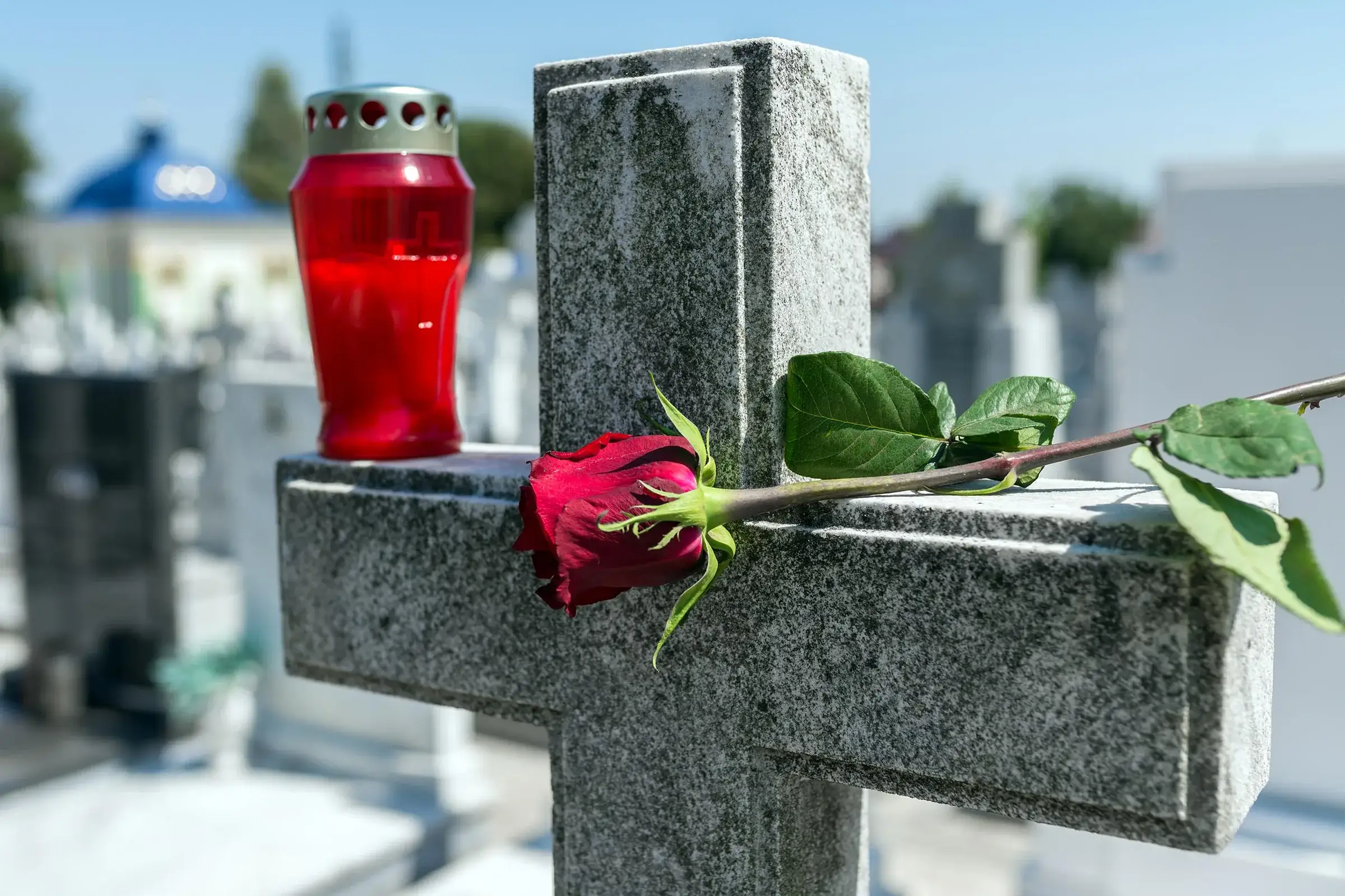 Cruce funerară din granit gri cu o candelă roșie și un trandafir