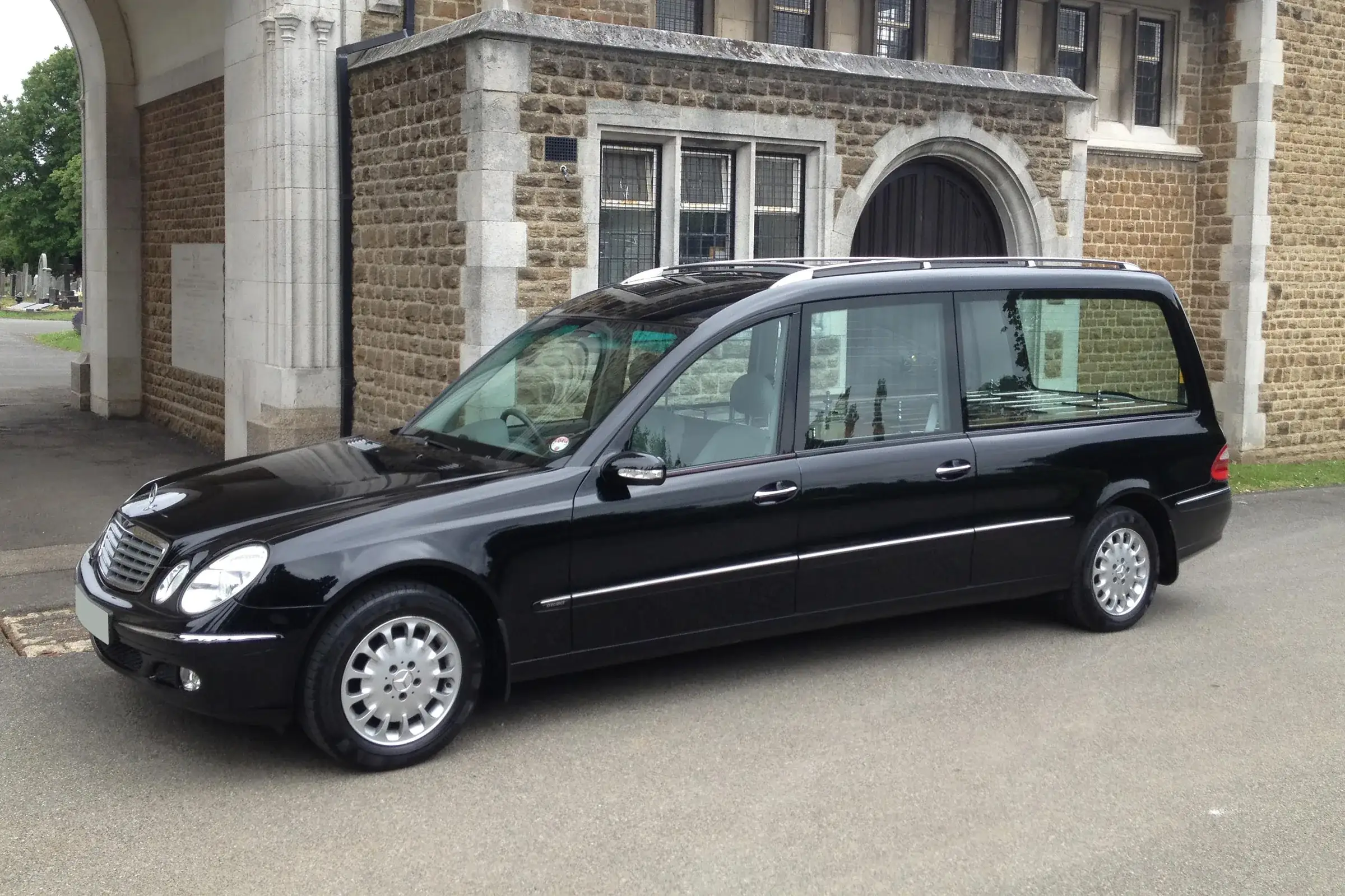 Mașină funerară neagră (dric) parcată în fața unei capele