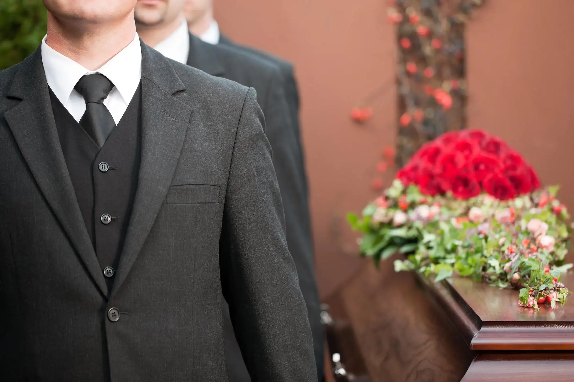 Personal al casei funerare Zgâmboi, în costum, lângă un sicriu decorat cu trandafiri roșii