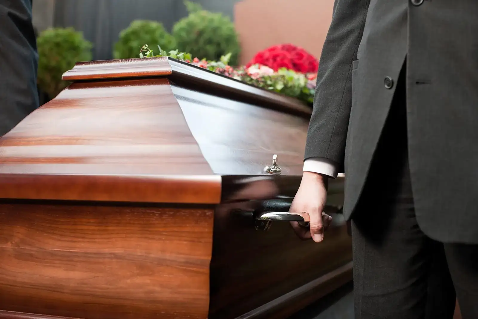 Membru al echipei funerare care poartă un sicriu din lemn lăcuit la o înmormântare